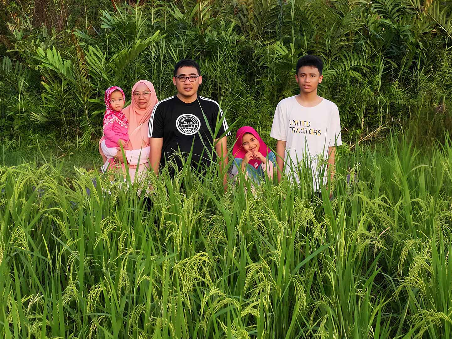 Keluarga berdiri bersama di tengah sawah saat sore hari, potret kehangatan rumah tangga sederhana dan penuh cinta.