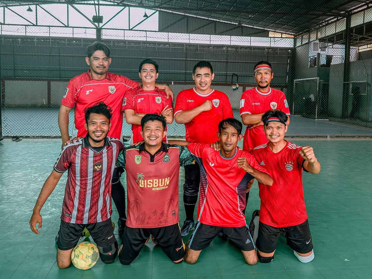Sekelompok teman tersenyum setelah bermain futsal bersama di sebuah lapangan indoor.